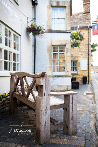Art print of a charming wooden park bench in a Cotswolds village in Gloucestershire, England. Travel photography.